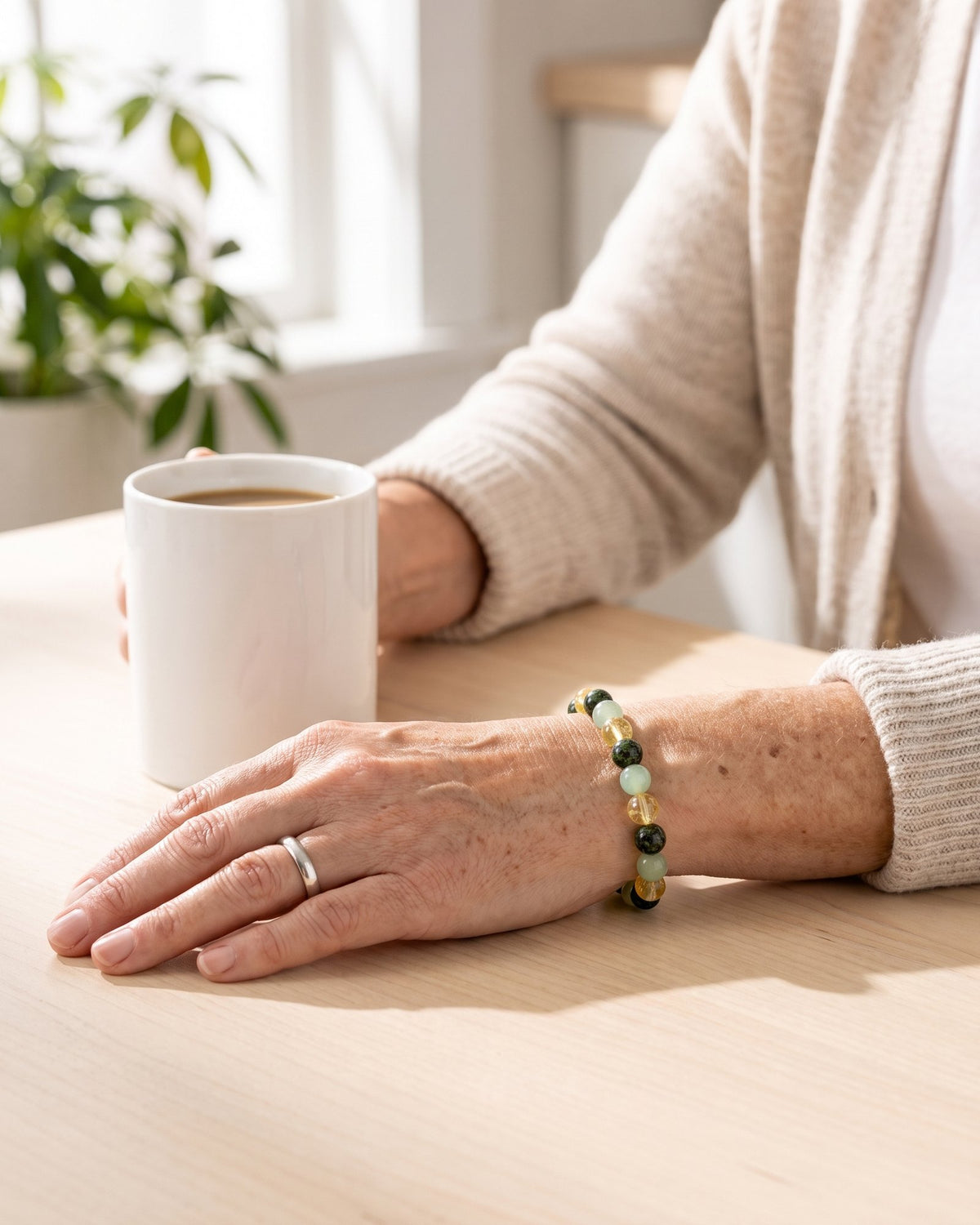 A woman's wrist wearing The Wealth Shift bracelet, resting on a table in morning light